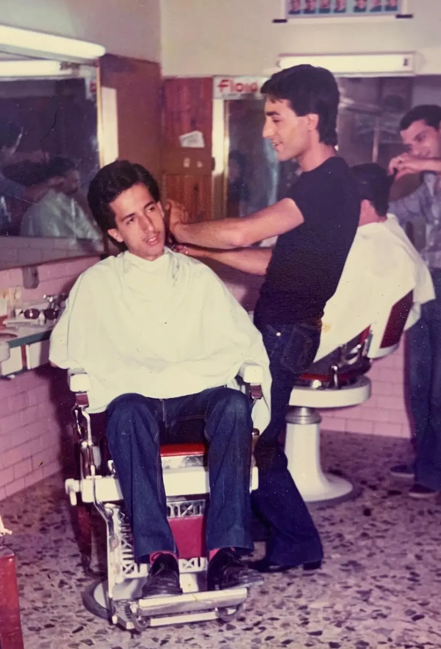 Gaspare Priolo, da giovane, taglia i capelli a un cliente seduto in poltrona, nella barberia dove lavorava.